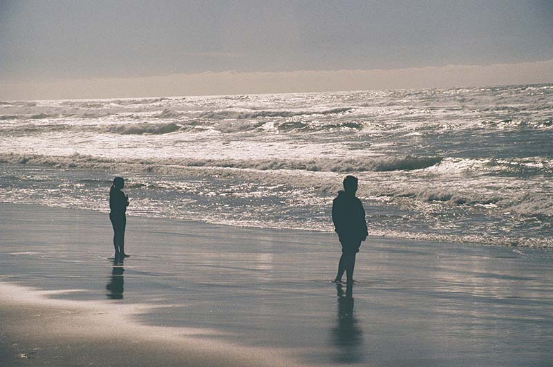 two standing at shore line watching ocean waves